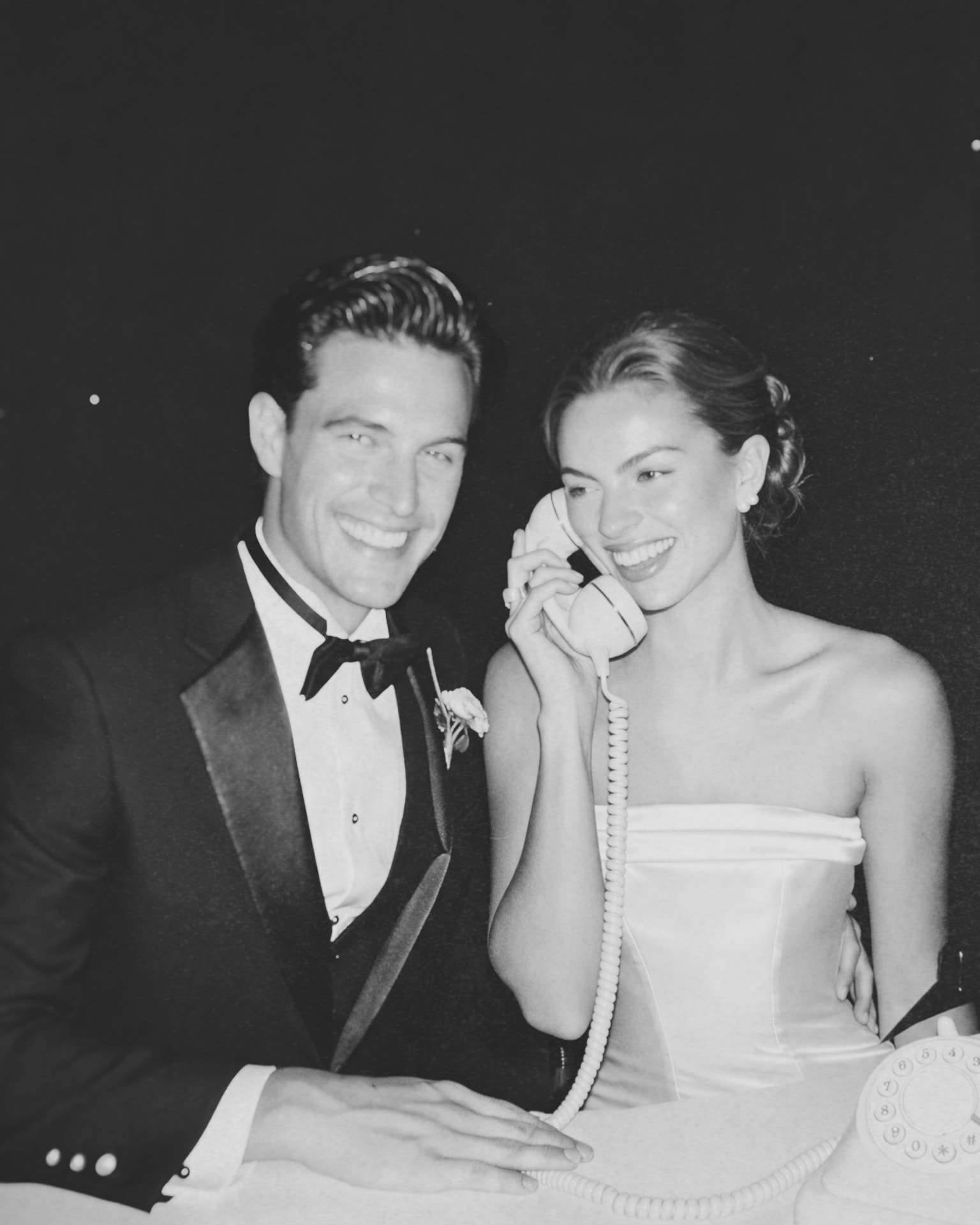 Casal de noivos sorrindo enquanto usa telefone retrô