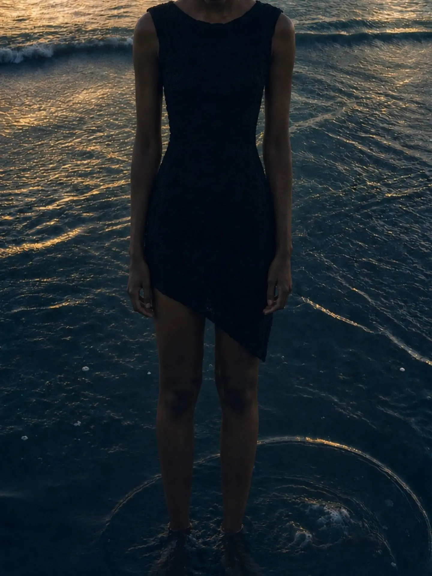 Modelo de vestido preto em pé na água ao pôr do sol