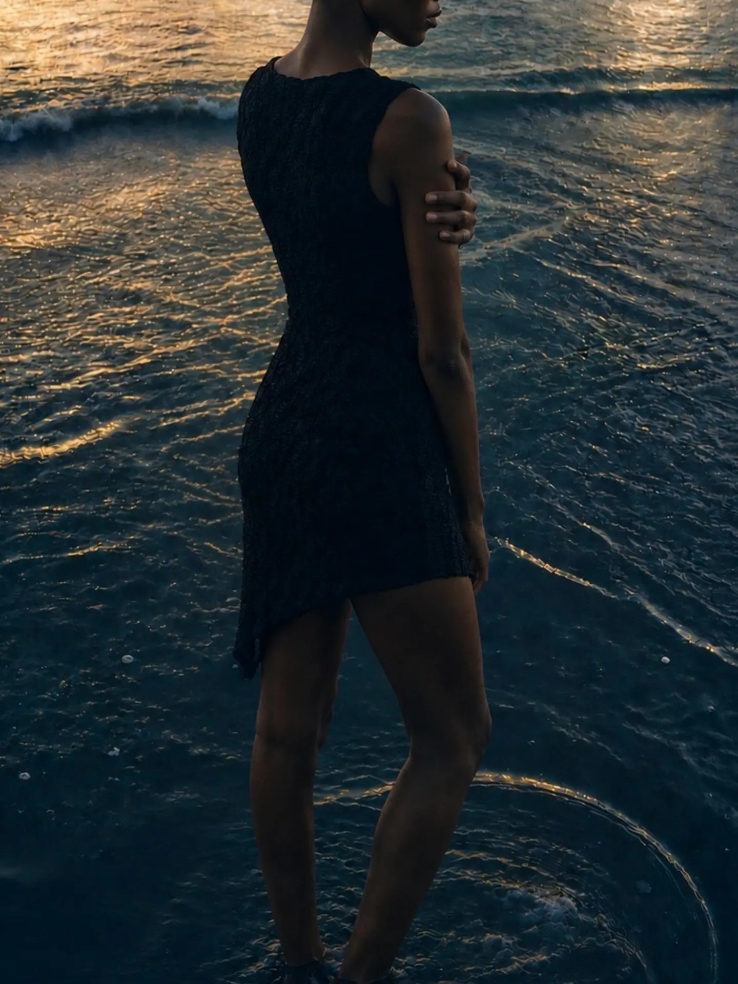 Modelo de vestido preto de perfil na água ao pôr do sol